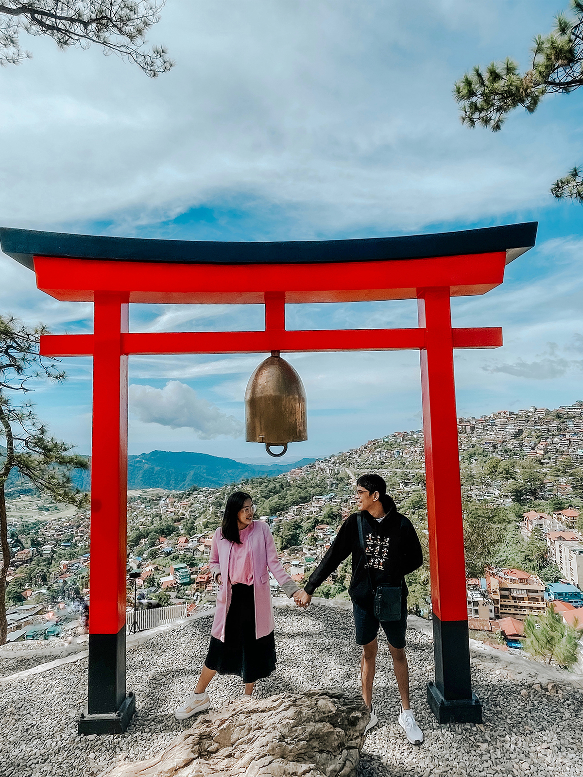 a couple under a torii gate overlooking Baguio City